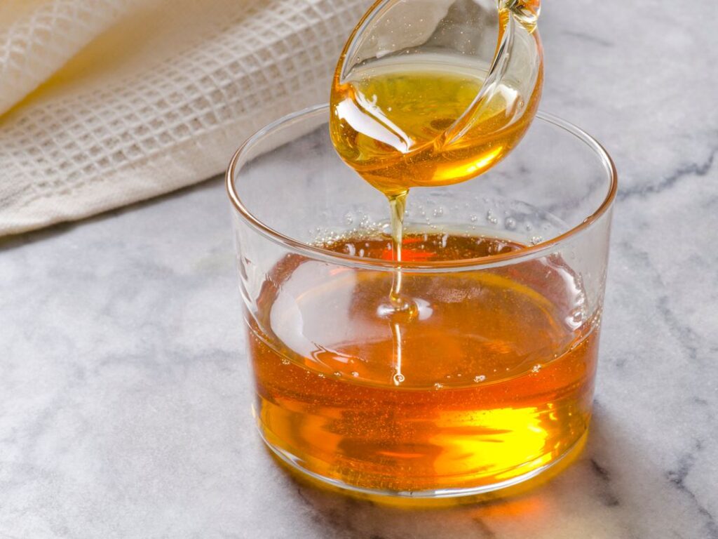 Syrup Secrets Unveileds.A clear amber liquid, likely whiskey, is elegantly poured from a glass decanter into a whiskey glass on a marble surface