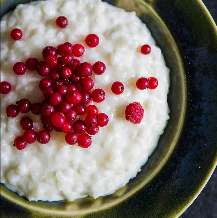 Creamy rice pudding in a bowl, garnished with fresh red currants and a raspberry,
