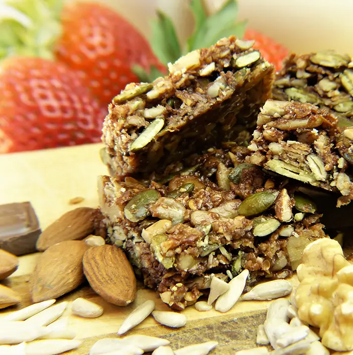 Homemade granola bar with a mix of oats, seeds, and nuts, presented on a wooden board, accompanied by fresh strawberries and assorted nuts scattered around.