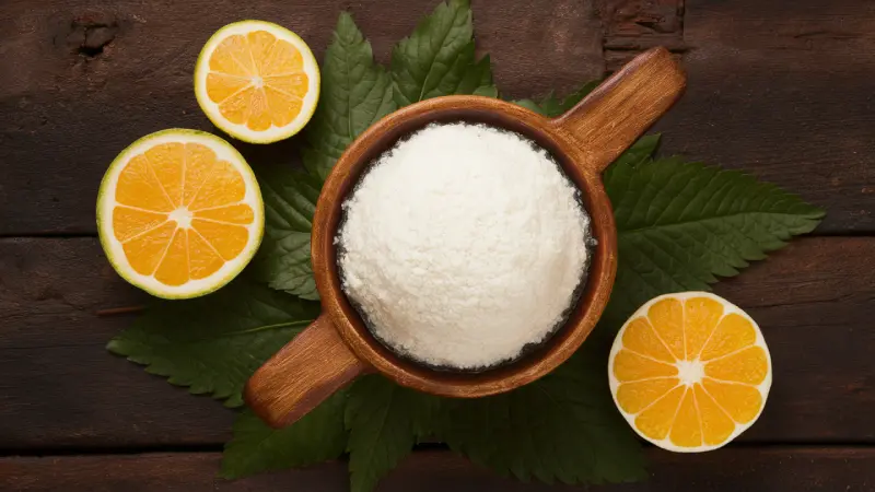 Tapioca Starch Benefits. A rustic wooden bowl filled with white salt, accompanied by vibrant green leaves and juicy orange slices, all arranged on a dark wooden surface, creating a natural and organic composition.