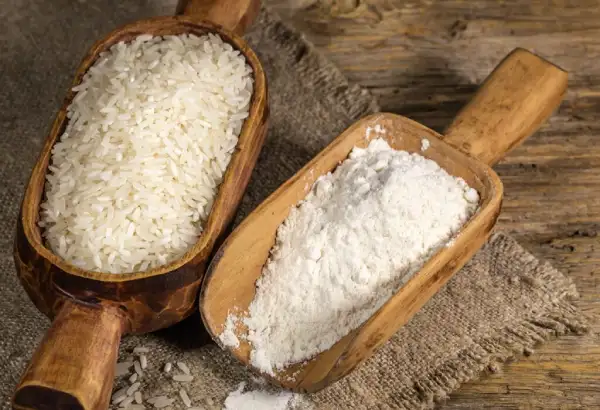 Vegan Drink Powder. Two wooden scoops on a rustic woven fabric, one filled with white rice and the other with white flour, surrounded by scattered grains of rice